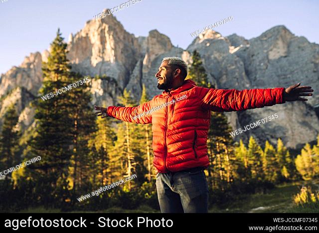 Smiling man with arms outstretched standing in front of Dolomites, Italy
