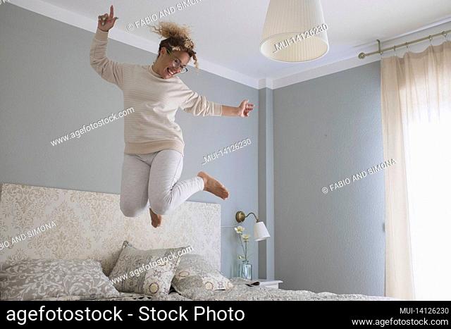 crazy young woman jumping on bed at home. overjoyed woman going crazy. carefree woman dancing and jumping on bed in excitement celebrating success at modern...