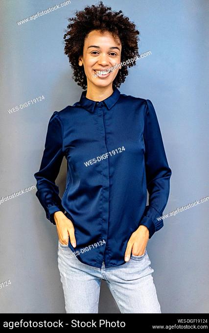 Smiling businesswoman with hands in pockets standing against blue background