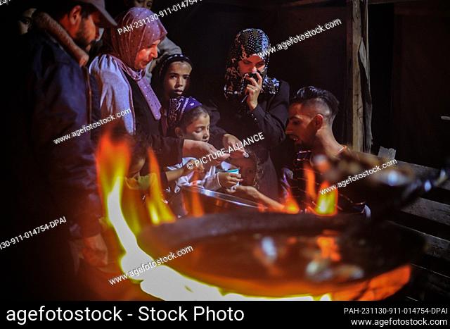 30 November 2023, Palestinian Territories, Khan Yunis: People gather around a Falafel vendor, who fries Falafel over a wood fire due to the lack of cooking gas