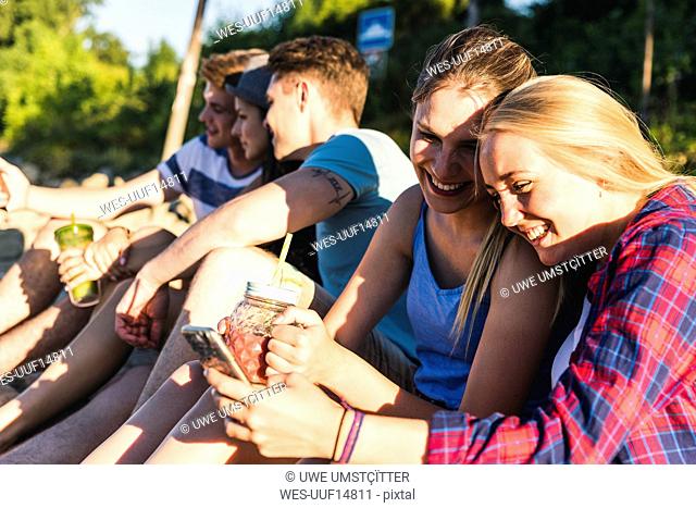 Group of happy friends sitting outdoors with refreshing drinks and cell phones