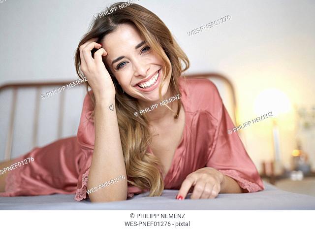Portrait of happy young woman in dressing gown lying in bed