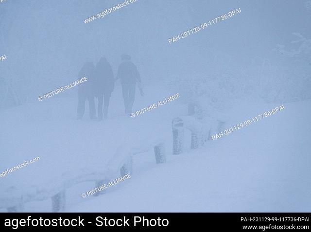 29 November 2023, Hesse, Glashütten: Walkers cross the Feldberg plateau through snow and fog in temperatures well below freezing