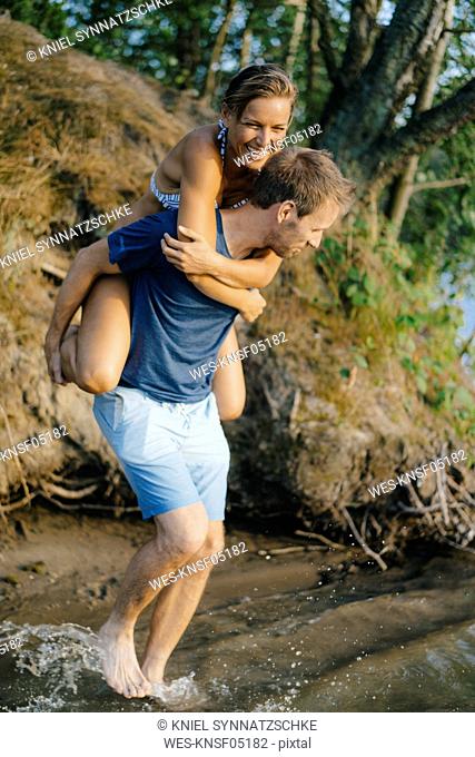 Happy man carrying girlfriend piggyback at a lake