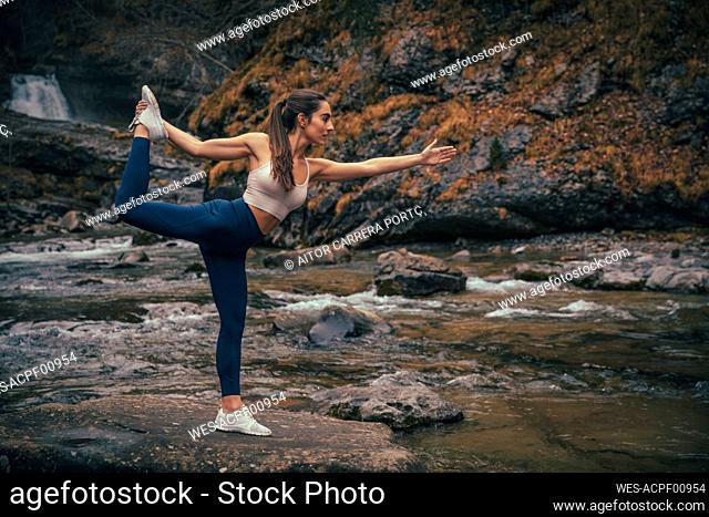 Athlete balancing while doing yoga by river in forest at Ordesa National Park, Huesca, Spain