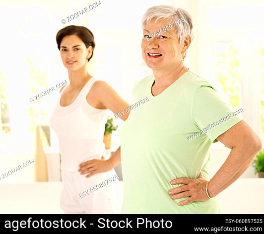 Healthy elderly woman doing exercises with personal trainer at home, smiling