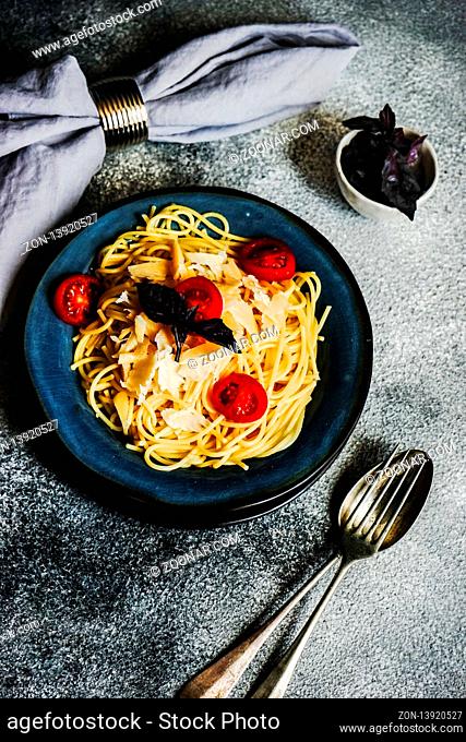 Italian pasta with cherry tomatoes and basil in a ceramic bowl on stone background with copy space