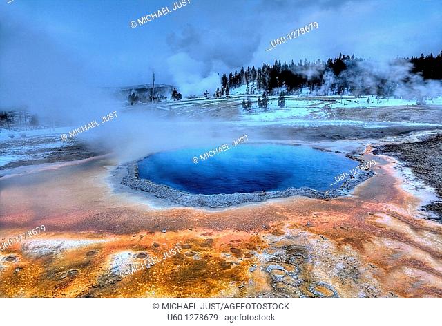 Crested Pool's colors shine during the winter at Yellowstone National Park as Grand Geyser erupts in the background