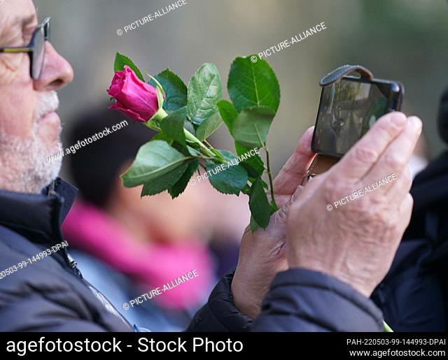 03 May 2022, Hamburg: A participant holds a rose in his hand and takes a photo of the wreath-laying ceremony at the memorial after the commemoration of the 77th...