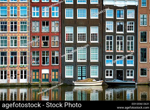 Row of typical houses and boat on Amsterdam canal Damrak with reflection. Amsterdam, Netherlands