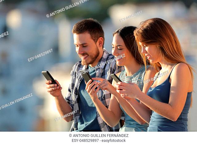 Group of three friends using their smart phones in a town outskirts