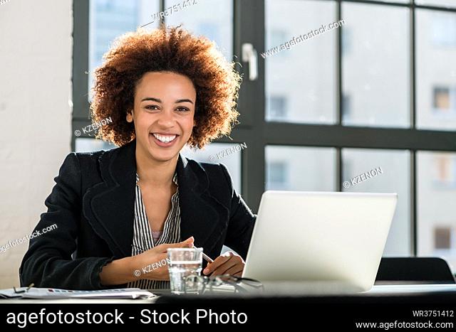 Portrait of African American woman sitting at desk while working on laptop in the office