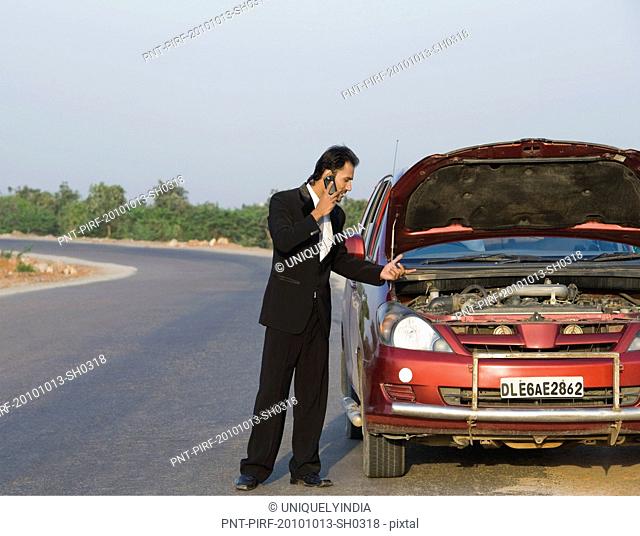 Businessman standing near a broken down car and talking on a mobile phone