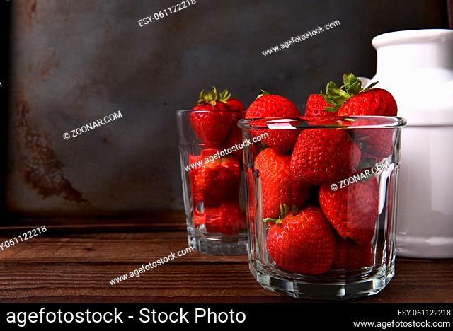 Horizontal still life with copy space of a glass filled with fresh picked strawberries on a wood table. In the background is a second glass of berries and a...