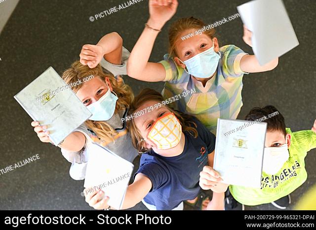 29 July 2020, Baden-Wuerttemberg, Friedrichshafen-Fischbach: Four pupils from the Fischbach primary school on Lake Constance hold up their certificates before...