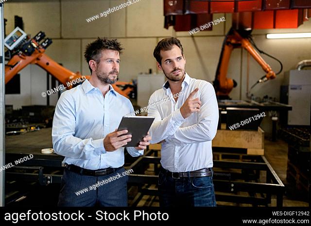 Businessman pointing while standing by colleague against automated robotic arm machine at factory