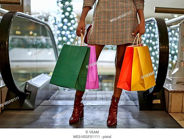 Happy black woman on a funny haircut holding colorful shopping bags in front of the escalator