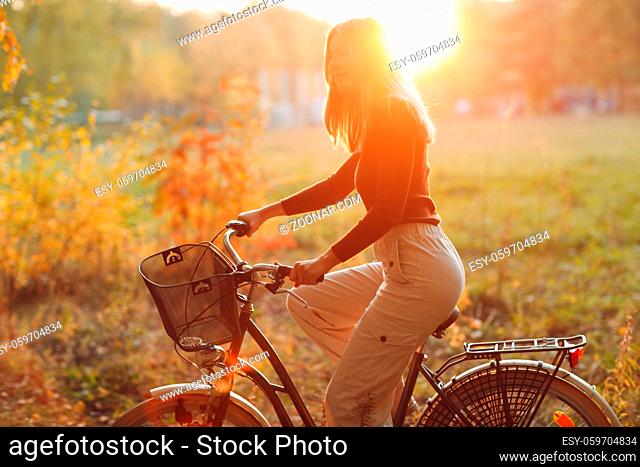 Happy active young woman riding vintage bicycle in autumn park at sunset