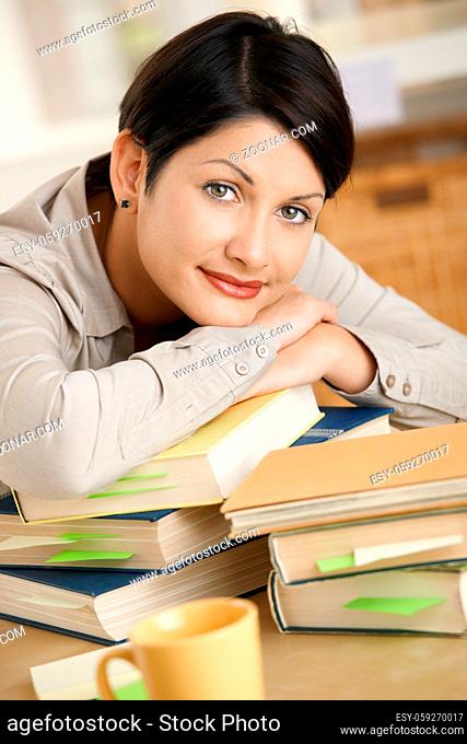 Tired young woman learning at home, resting on pile of books