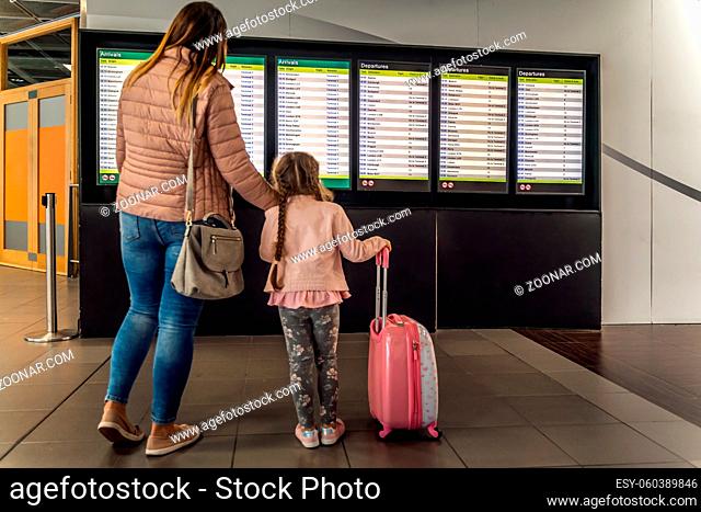 Defocused silhouette of family, young girl and her mother on airport terminal. Checking arrival and departure board for their flight. Dublin, Ireland