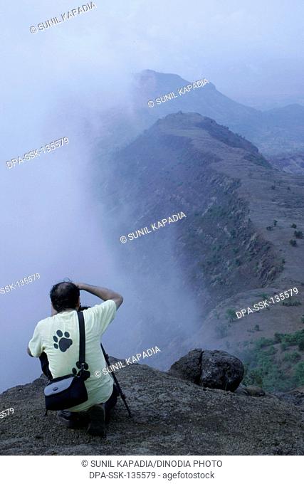 A photographer taking a picture of a landscape with monsoon clouds rising from the valley Matheran ; Maharashtra ; India