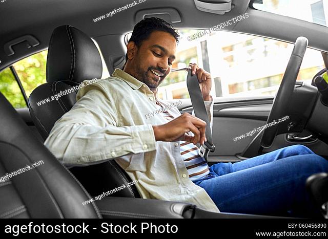 smiling indian driver fastening seat belt in car
