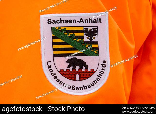 04 December 2023, Saxony-Anhalt, Niedere Börde: ""Landesstraßenbaubehörde Sachsen-Anhalt"" is written on a patch on the jacket of a participant in a symbolic...