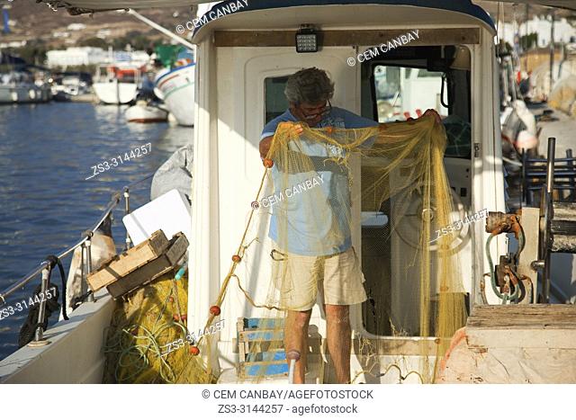 Fisherman mending nets in his traditional fishing boat at the harbour of the Naoussa village, Paros Island, Cyclades Islands, Greek Islands, Greece, Europe