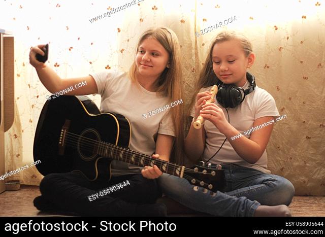 Two female teens playing musical instruments and making selfie sitting on the floor at home, youth hobby and leisure concept
