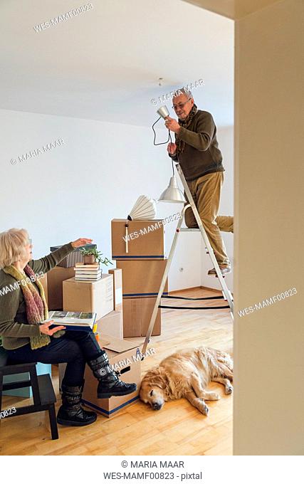 Senior couple in a new home with man mounting ceiling lamp