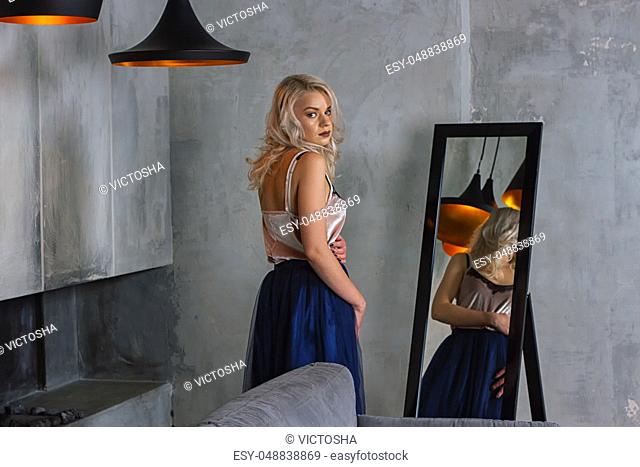 Young beautiful woman in cocktail dress standing near mirror