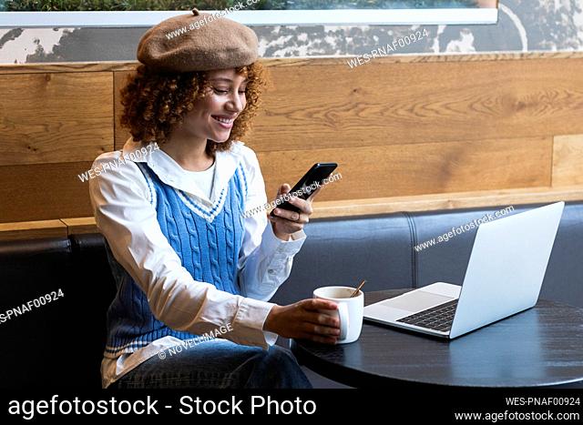 Female teenager having coffee while using mobile phone at cafe