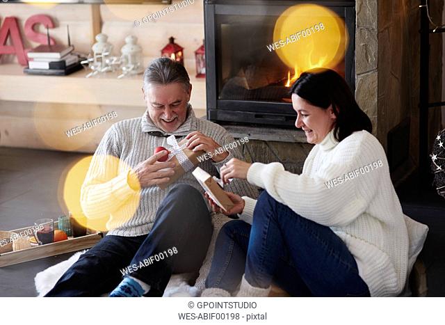 Happy mature couple at the fireplace unpacking gifts