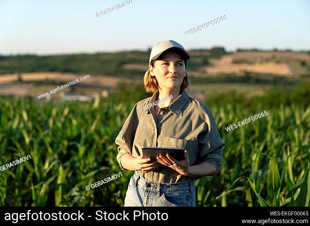 Woman standing with digital tablet in field looking around
