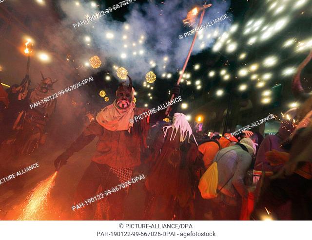 21 January 2019, Spain, Palma: A man disguised as a demon, holding fireworks, walks among the people during the traditional Correfoc (firewalk or street...