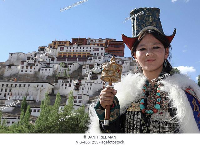 INDIA, THIKSEY, 09.07.2014, A young Ladakhi woman wearing a traditional Koshian costume and praying using a prayer wheel with the Thiksey Gompa (Thiksey...