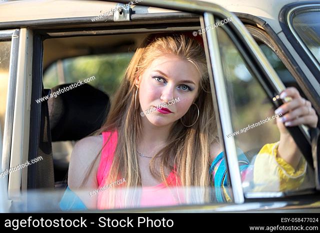 A beautiful blonde girl with long hair looks out of the car window