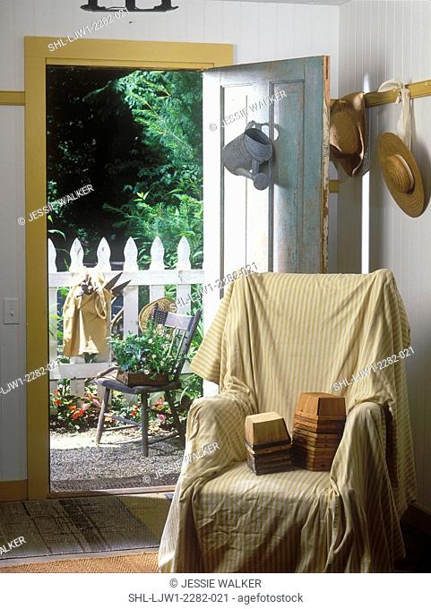 ENTRANCEWAYS: Converted garage, covered wingchair, stacks of berry baskets on chair, hooks holds garden hats, blue distressed door to outside garden area