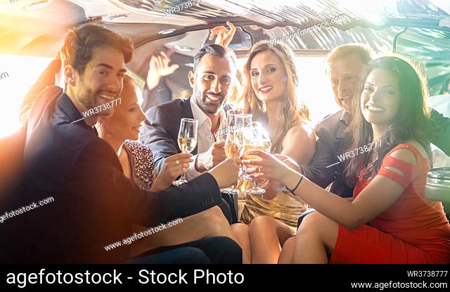 Group of women and men clinking glasses in a limousine having fun and being happy