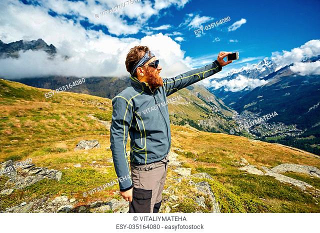 hiker at the top of a pass enjoy sunny day in Alps and take photo on smartphone. Switzerland, Trek near Matterhorn mount