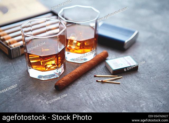 Carafe of Whiskey or brandy, glasses and box of finnest Cuban cigars on an gray stone table. With ice cubes