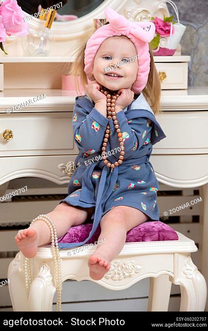 A cute little girl is sitting at the dressing table and holding beads