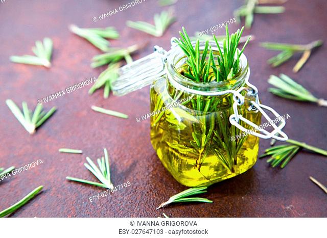 Rosemary oil. Rosemary essential oil jar glass bottle and branches of plant rosemary with flowers on rustic background