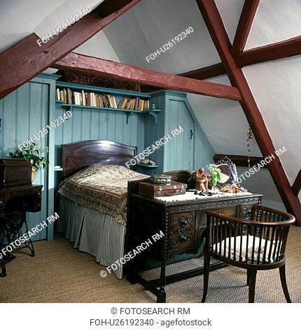 Mahogany bed below shelves in alcove on blue panelled wall in attic bedroom with small antique desk and chair