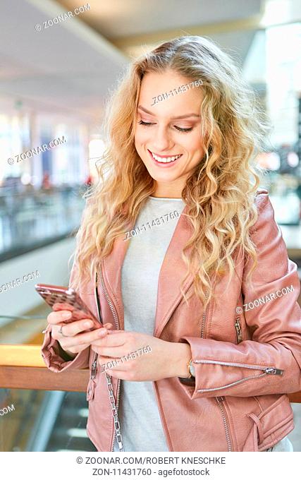 Junge blonde Frau liest eine SMS Nachricht auf dem Handy und freut sich