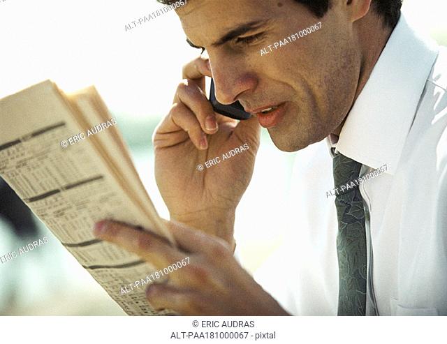 Businessman using cell phone and looking at newspaper, close-up, side view