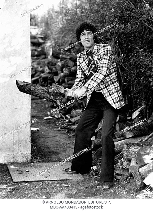 Ninetto Davoli with a log in his hands. Italian actor Ninetto Davoli using a log as a baseball bat. Rome, 1970s