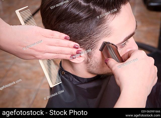 Closeup picture mas#39;s hairstyling and haircutting with hair clipper by barber girl or hairdresser in barber shop or hairdressing salon