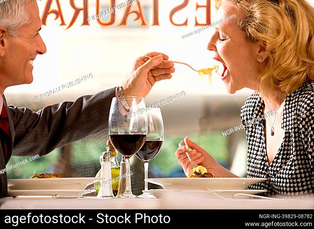 Man feeding pasta to woman