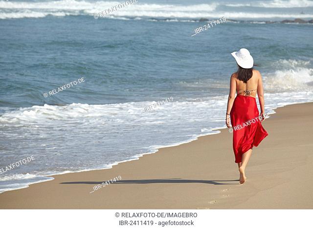 Rear view of a young woman wearing a bikini and a red sarong walking along a beach in summer, Arcachon, Aquitaine, France, Europe